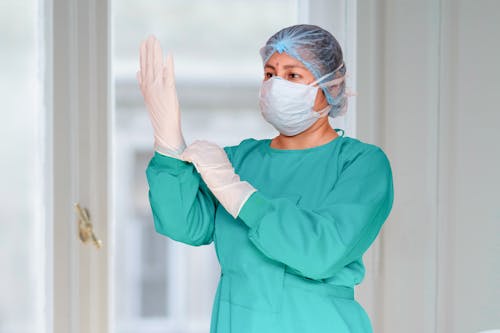 Woman in Teal Scrub Suit With White Surgical Mask and Gloves