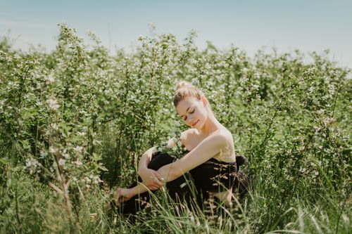 Free Young woman in a black tube top sitting among blooming flowers in a sunlit field. Stock Photo