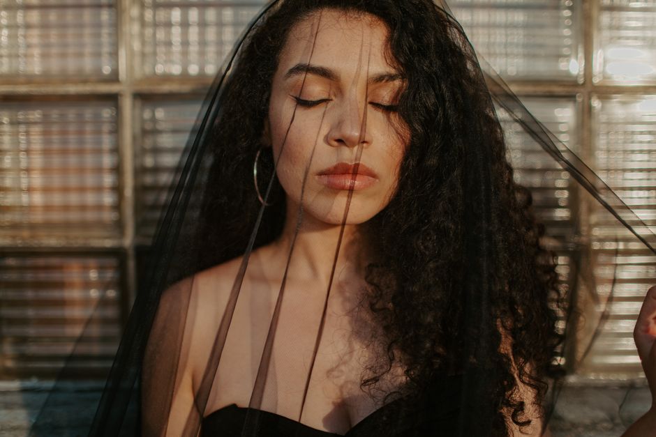 Portrait of a woman with curly hair and veil, eyes closed in serene expression.