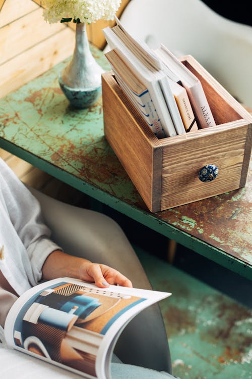 Free Person Looking At A Magazine Beside A Wooden Box Of Books Stock Photo