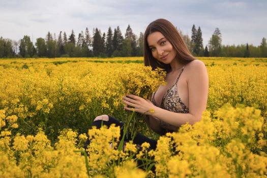 Young woman sitting in a vibrant yellow flower field, smiling and holding flowers.