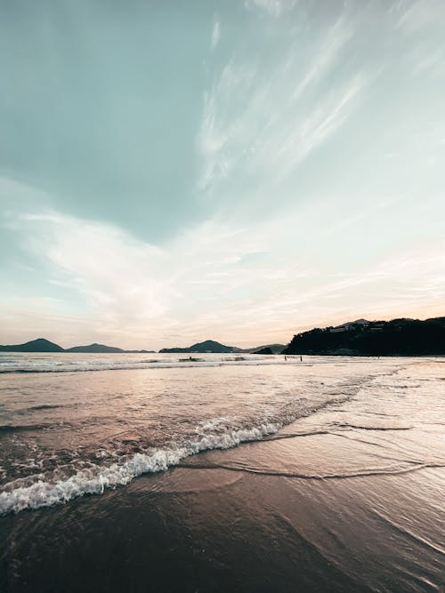 Wonderful sunset seascape with sandy coastline and foamy waves against rocky valley with cloudy blue sky