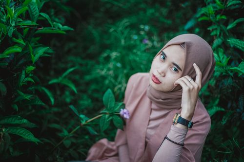 Free A woman wearing a pink hijab sits amidst lush green plants, exuding serenity. Stock Photo