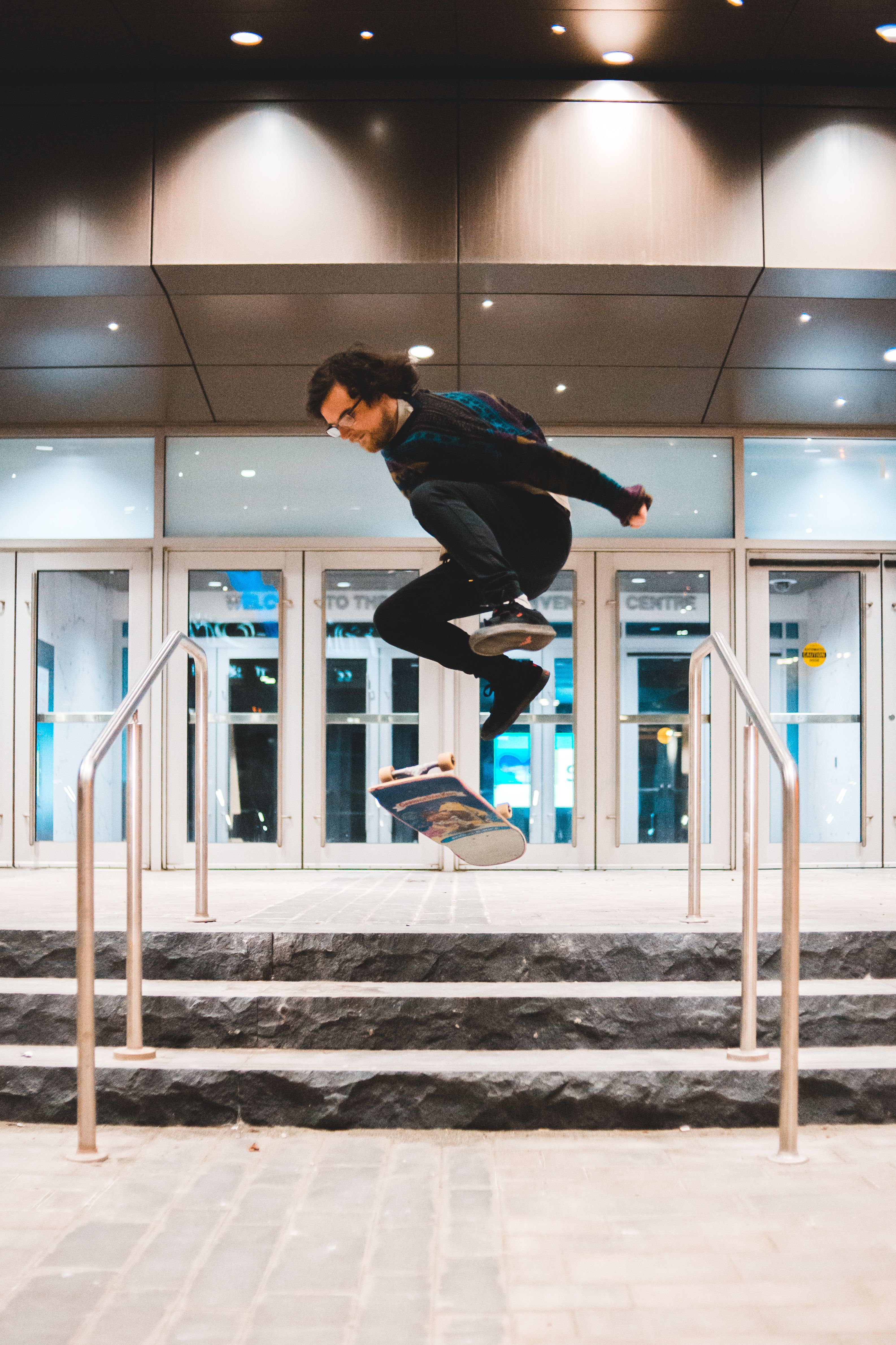 An adult male skateboarder executing an ollie on stairs in an urban environment at night.