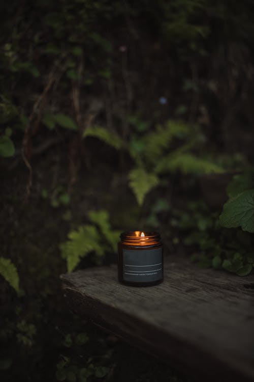 A Lighted Candle in a Gray and Brown Jar on a Wooden Surface