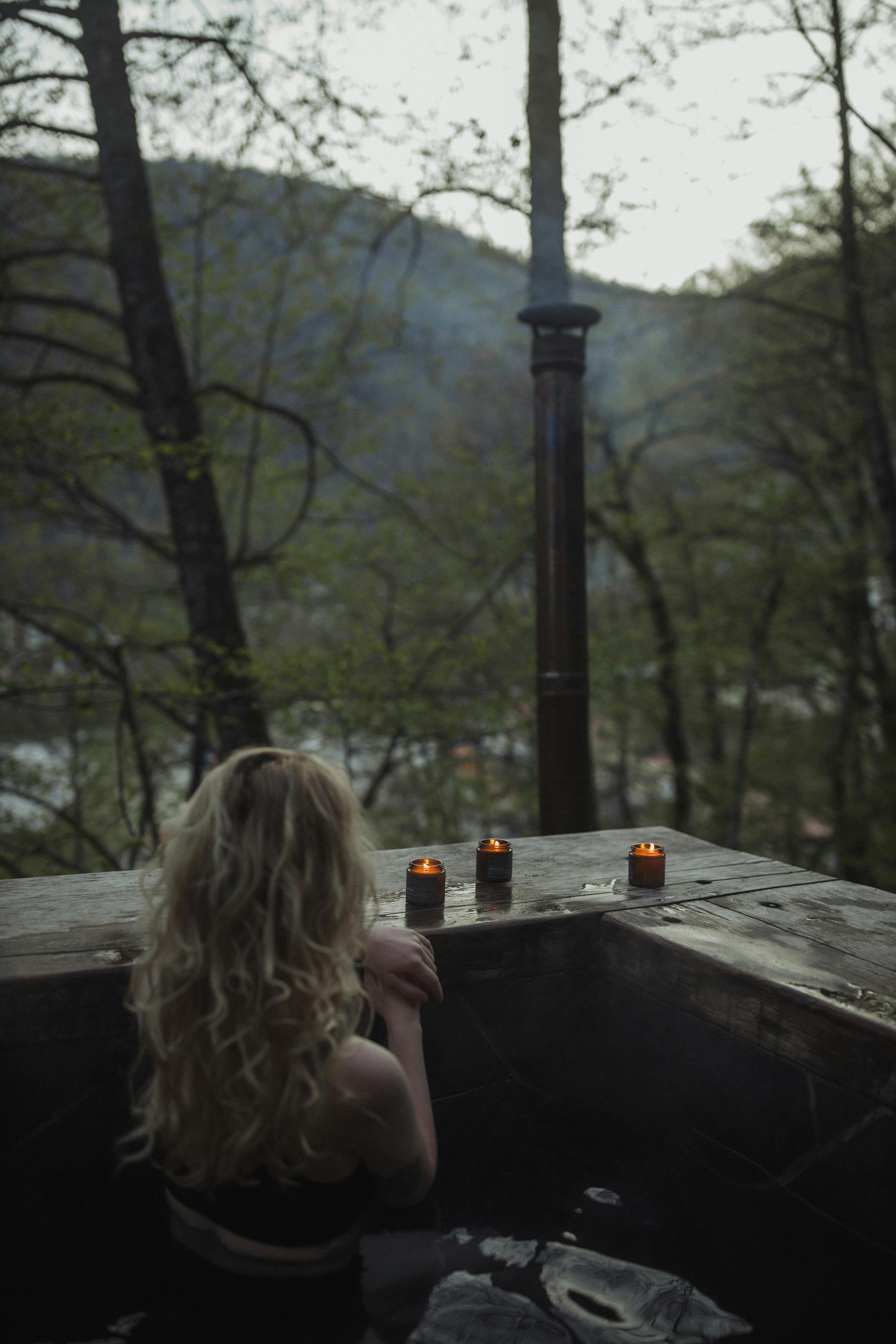 A woman relaxes in an outdoor bath surrounded by nature, illuminated by candlelight.