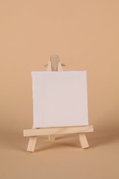 Minimalist image featuring a blank canvas on a small wooden easel set against a beige backdrop.