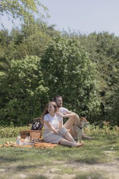 在一个阳光明媚的日子里，一对白人夫妇带着他们的狗，在郁郁葱葱的公园里轻松地野餐
