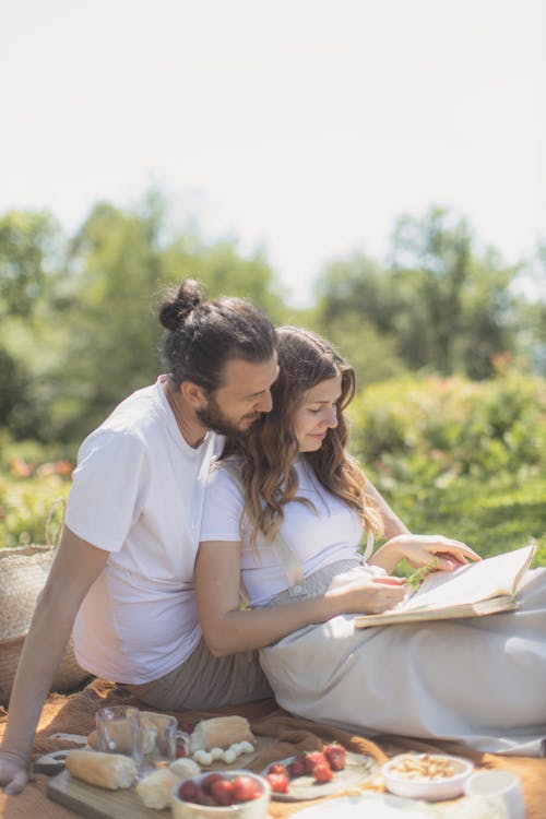 Free A Couple Reading a Book Sitting Together on a Picnic Mat Stock Photo