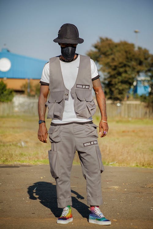 Man in Gray Vest and Pants Wearing Black Face Mask and Black Hat Standing on the Ground