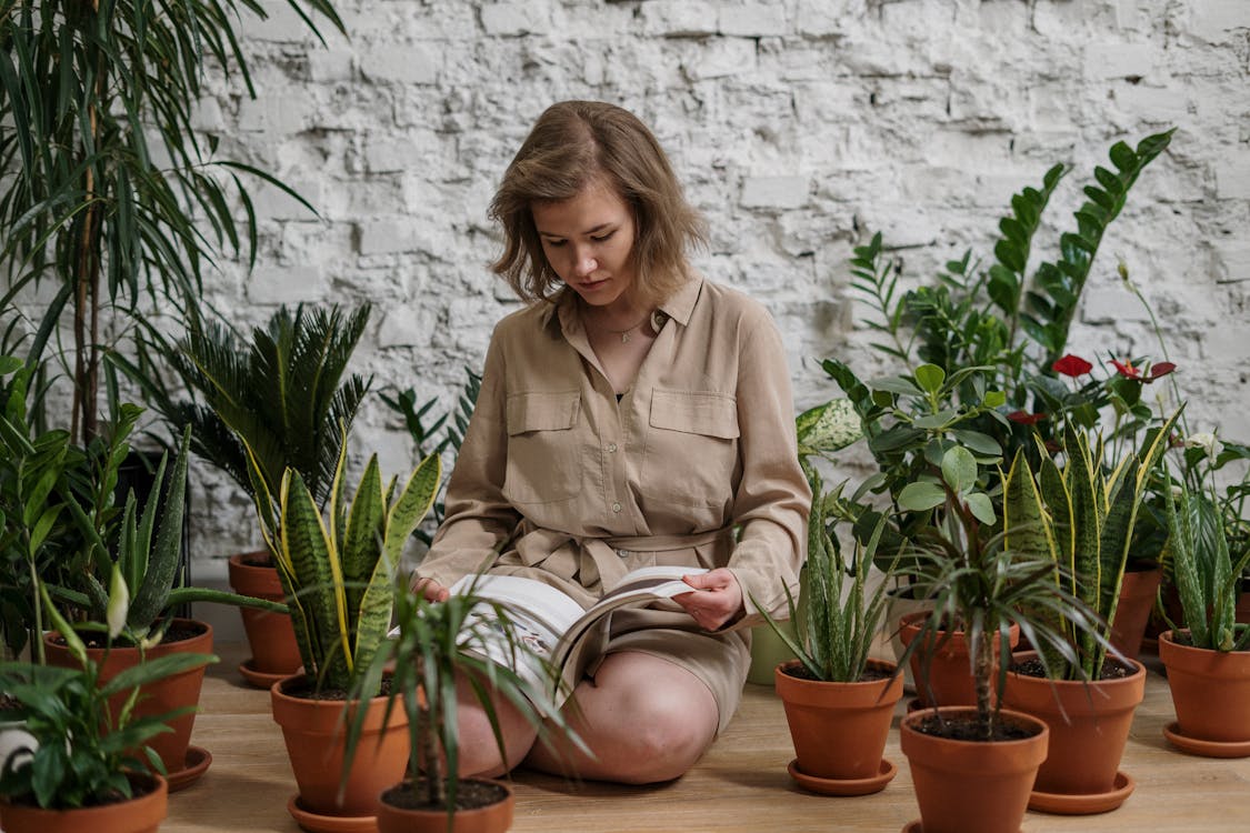 Free Woman Sitting While Reading Book Near Potted Plants Stock Photo