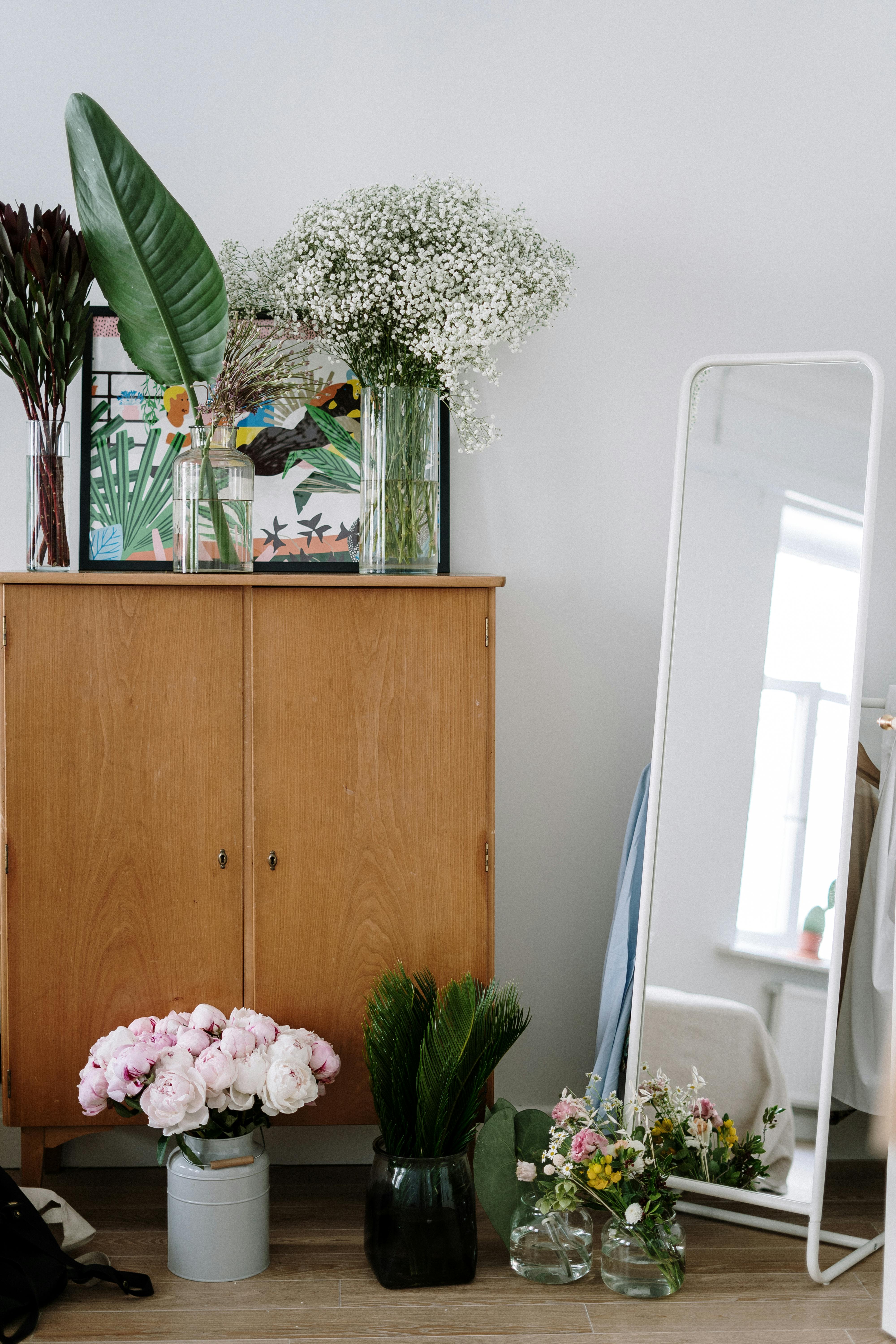 Stylish home decor with various flower arrangements and a standing mirror.