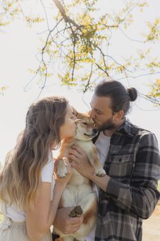 一对恩爱的夫妇在户外亲吻他们的柴犬，捕捉到了深情与陪伴的时刻