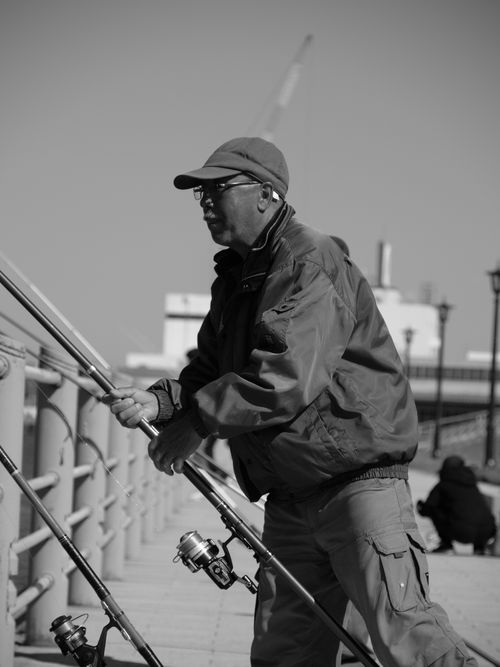 Free Black and white side view of senior ethnic male in cap catching fish with fishing rod near fence Stock Photo