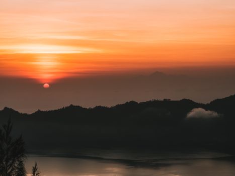 Capture the stunning Bali sunset with vivid orange skies and tranquil lake reflections.