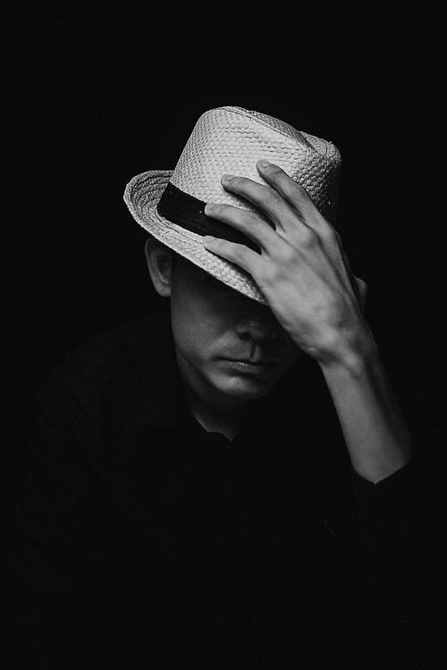 Free Black and white of anonymous male touching trendy straw hat while standing in dark room Stock Photo
