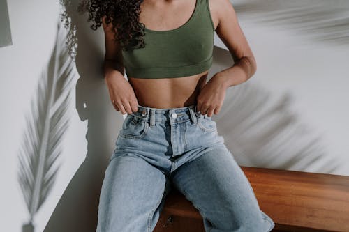 Woman in Green Tank Top and Blue Denim Jeans Sitting on Brown Wooden Bench