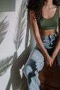 阳光下，穿着牛仔布的女人坐在墙上，热带植物的影子映在墙上