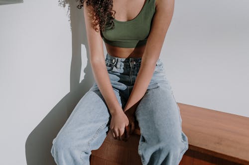 Woman in Green Tank Top and Blue Denim Jeans Sitting on Brown Wooden Chair
