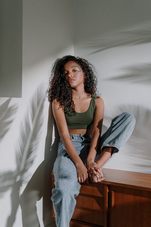 Woman in Black Tank Top and Blue Denim Jeans Sitting on Brown Wooden Table