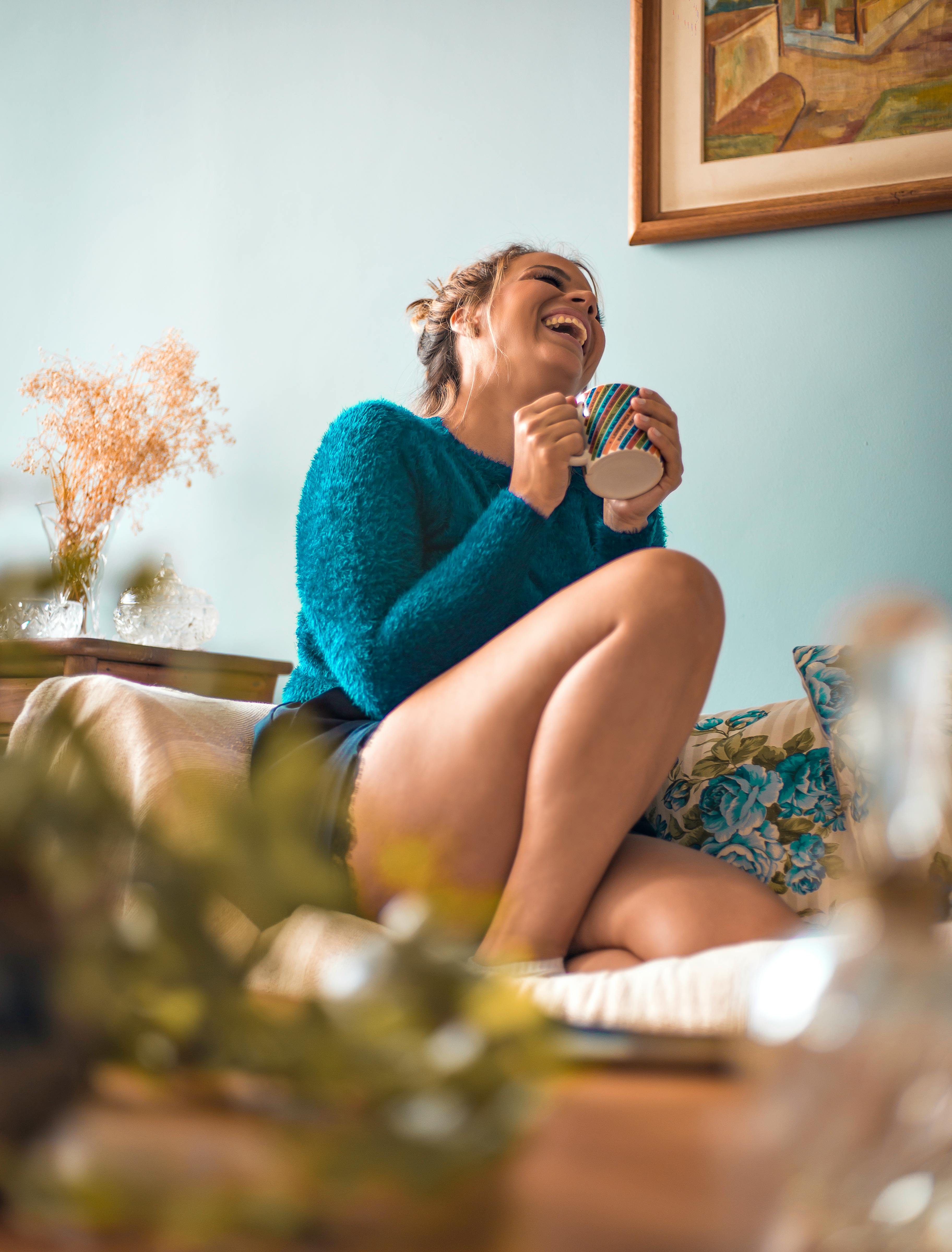 快乐的女人在舒适的客厅里边喝热饮边笑