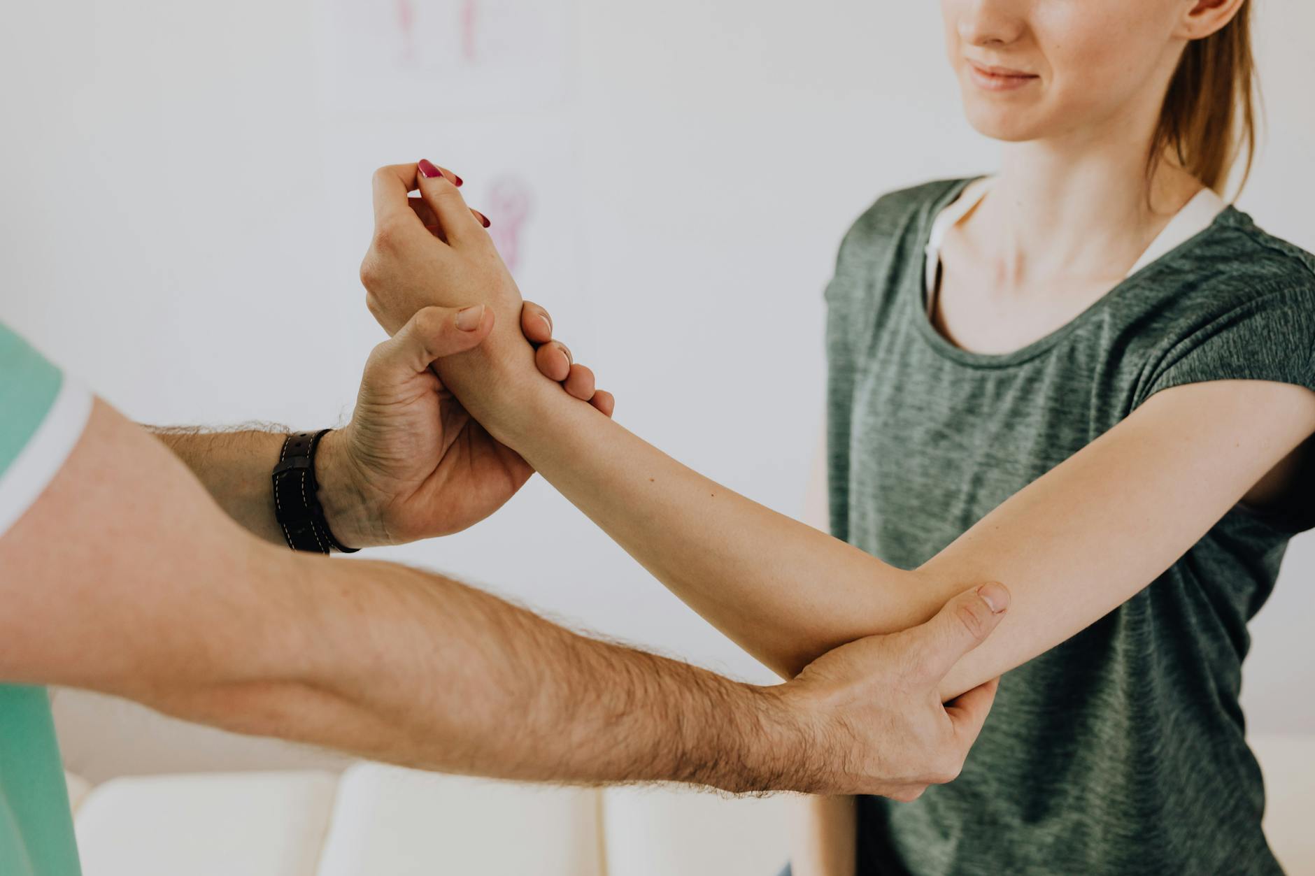 Crop unrecognizable chiropractor examining arm of smiling female patient