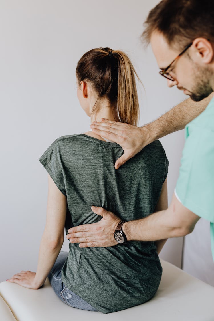 Crop Osteopath Examining Back Of Anonymous Woman In Doctor Office