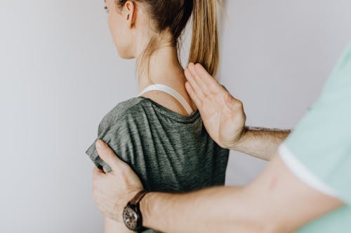 Free Back view of crop unrecognizable osteopath in uniform and wristwatch checking up back of slim female patient in casual wear on white background Stock Photo