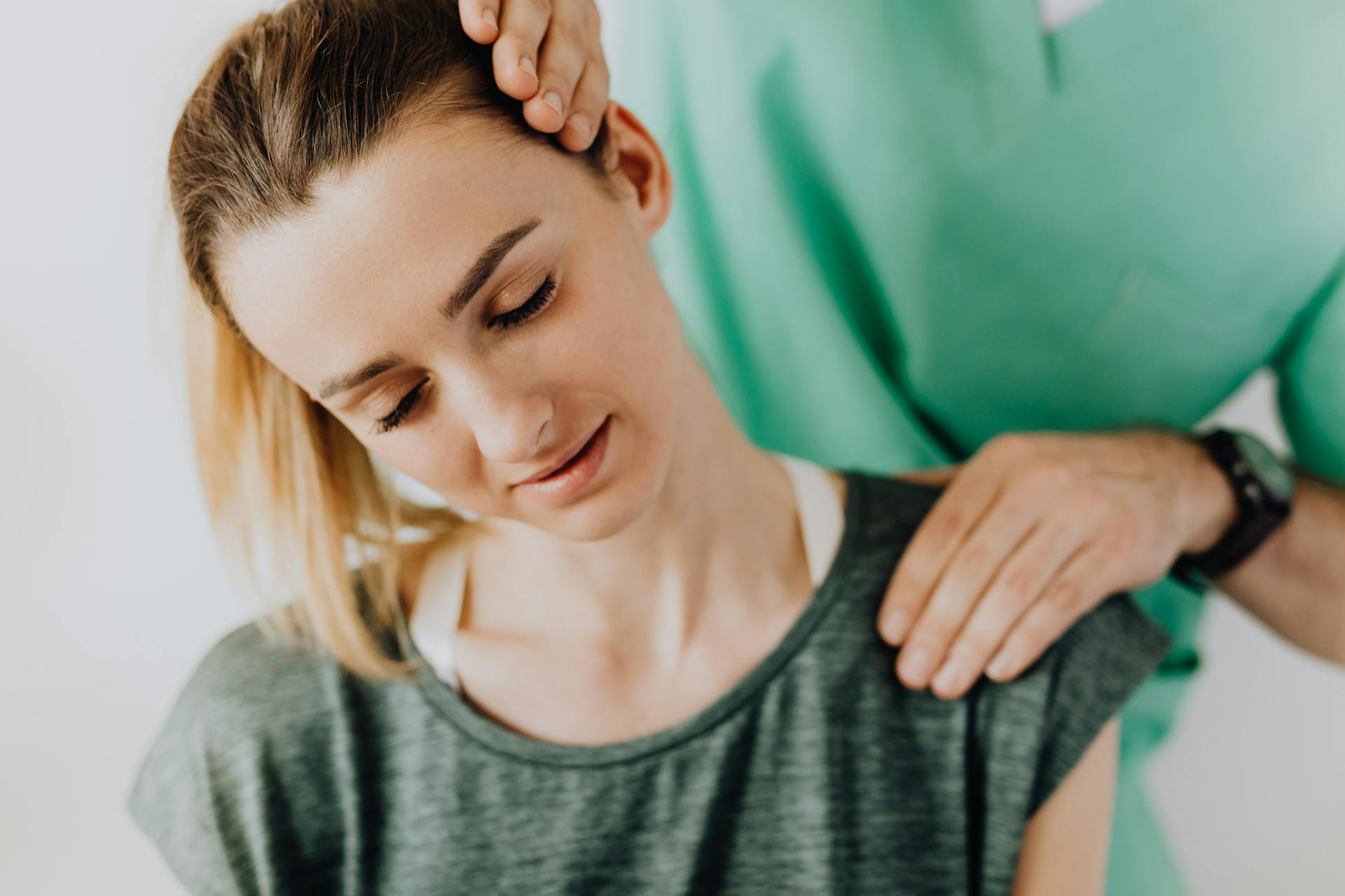 Crop professional male massage therapist in green medical uniform doing therapeutic neck massage on content female patient wearing casual clothes