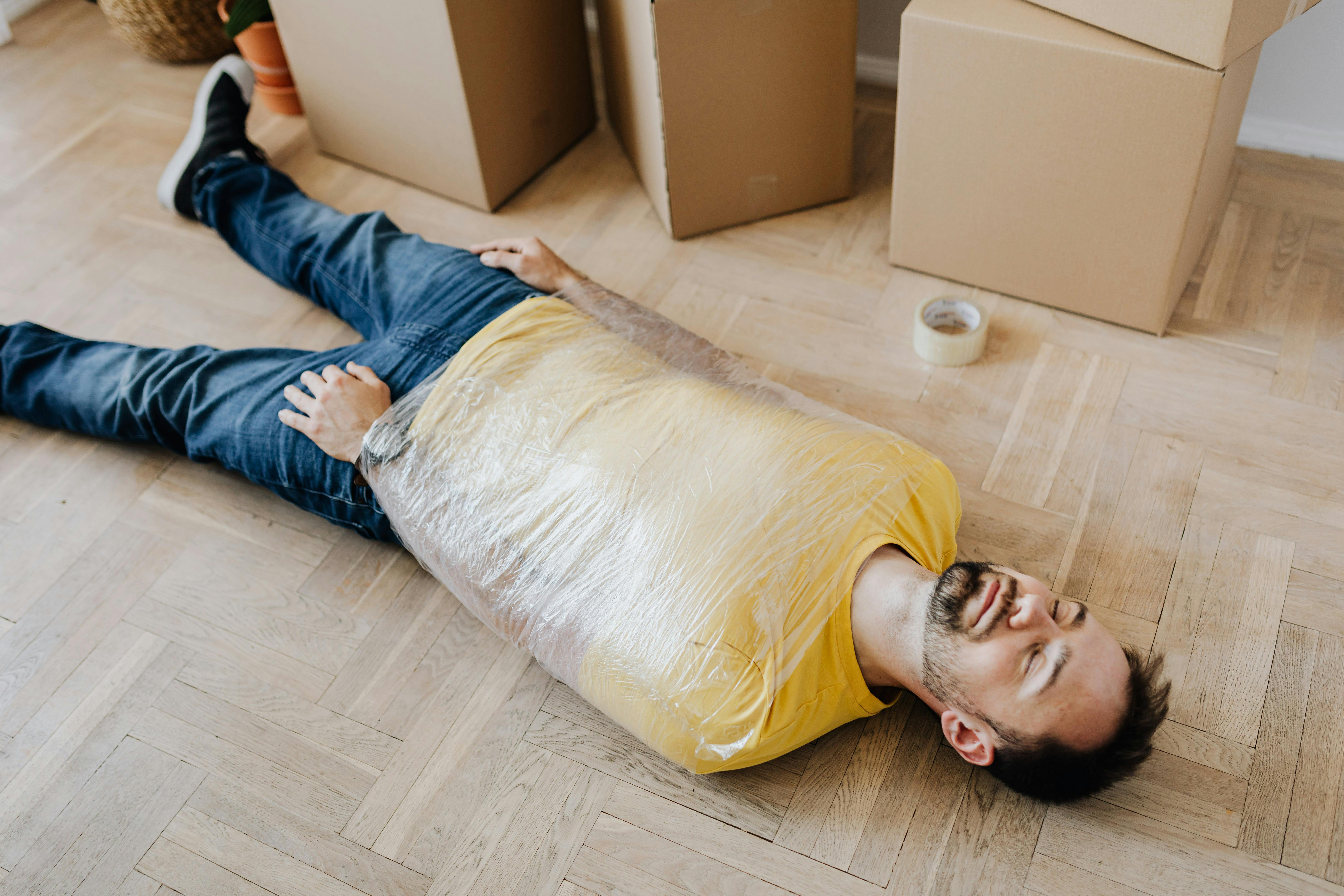tired man wrapped in plastic film lying on floor