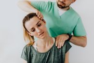 男性按摩师轻轻按摩女性患者的颈部和肩部，同时拉伸其颈部肌肉