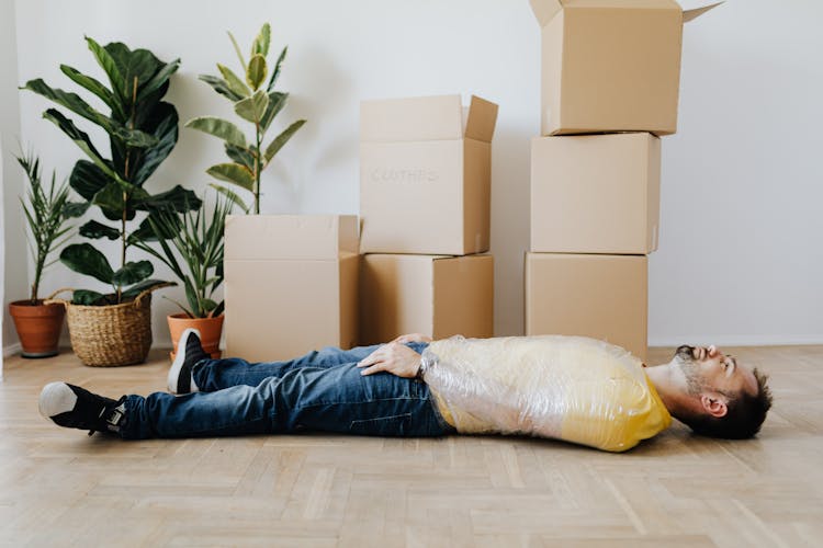 Calm Man Wrapped In Plastic Tape Near Carton Boxes