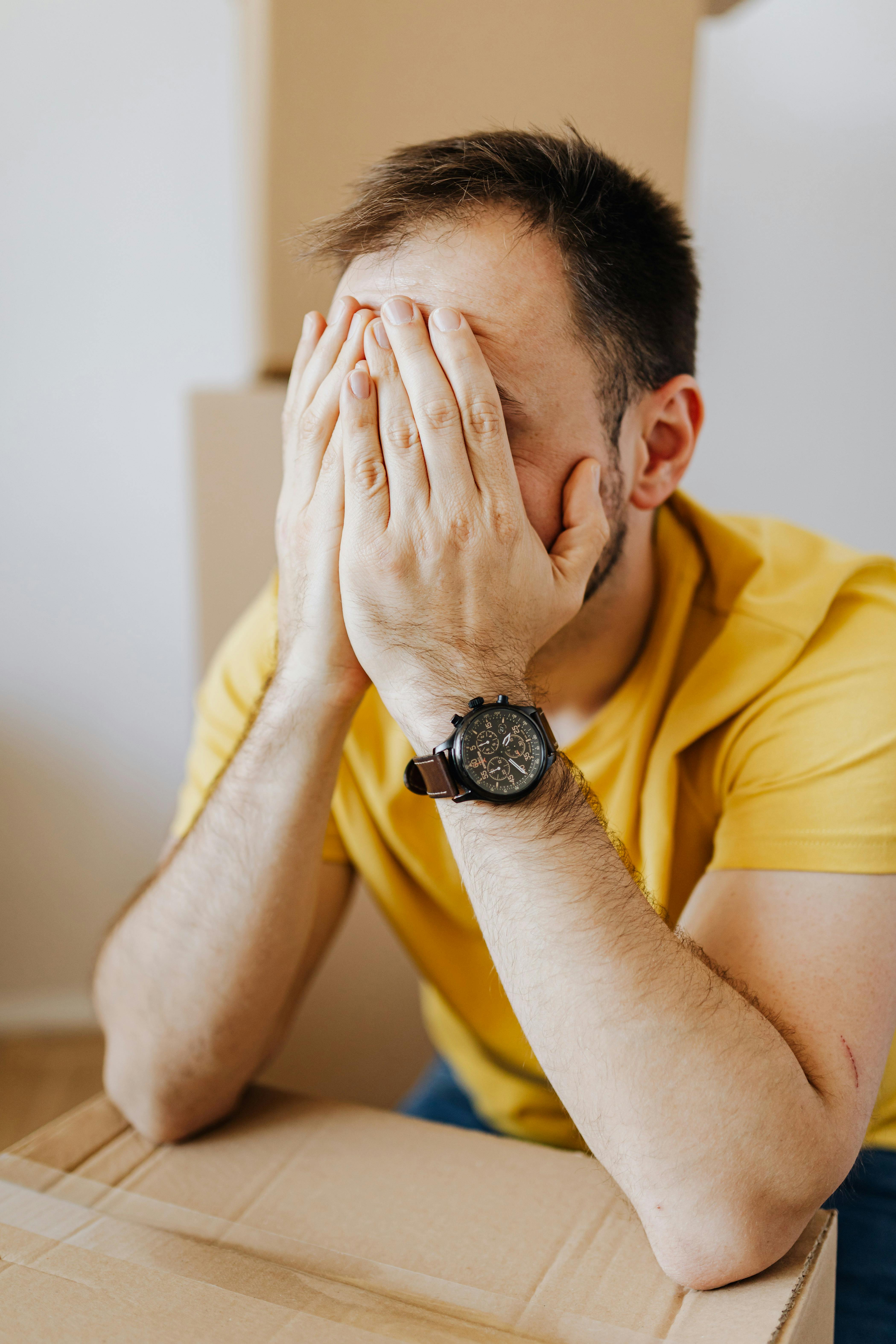 dissatisfied man covering face and leaning on carton box