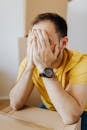 Dissatisfied man covering face and leaning on carton box