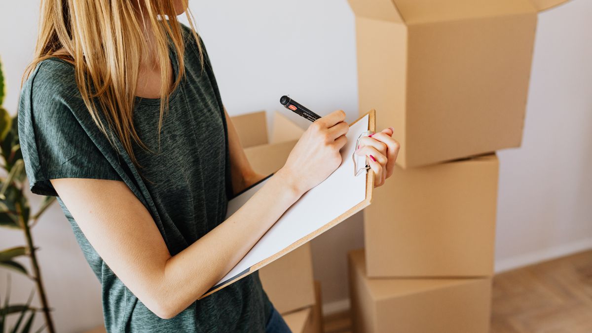 Side view crop female wearing casual shirt standing near packed cardboard containers and taking notes before relocation into new modern place