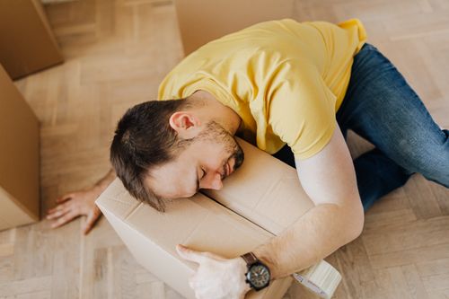 Free High angle of fatigued male in casual wear sleeping on floor with cardboard box after packing belongings before moving out Stock Photo