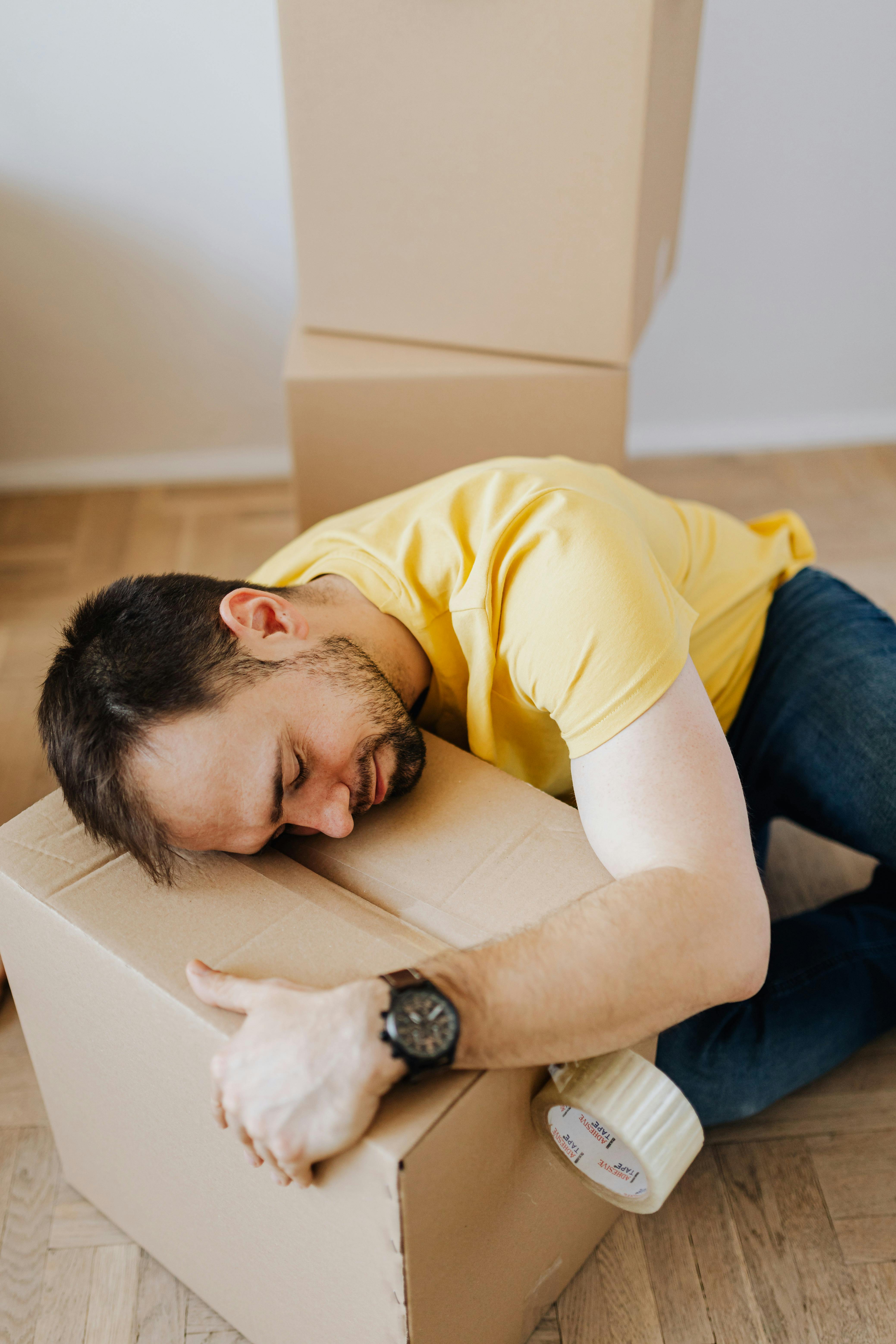 fatigued young man lying asleep on floor with carton box