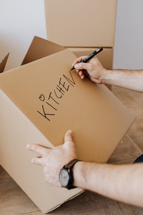 Crop man writing on carton box word kitchen