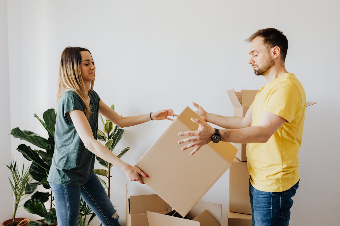 Free Side view serious couple wearing jeans and shirts carrying cardboard boxes with belongings while moving into new apartment together Stock Photo