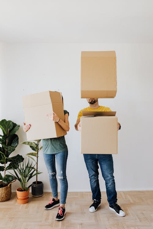 Full body anonymous couple in casual clothes carrying and playing with carton boxes in excitement during relocation into new flat