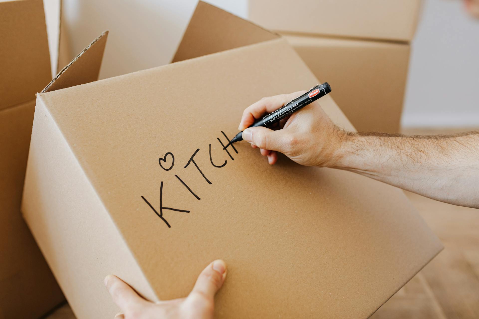 From above of unrecognizable adult male writing with black marker on cardboard containers while packing staff and preparing for relocation in new home