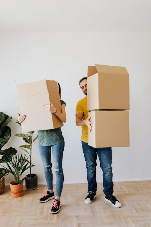 Adult woman and man wearing casual clothes standing near potted plants with cardboard containers while moving to new house together