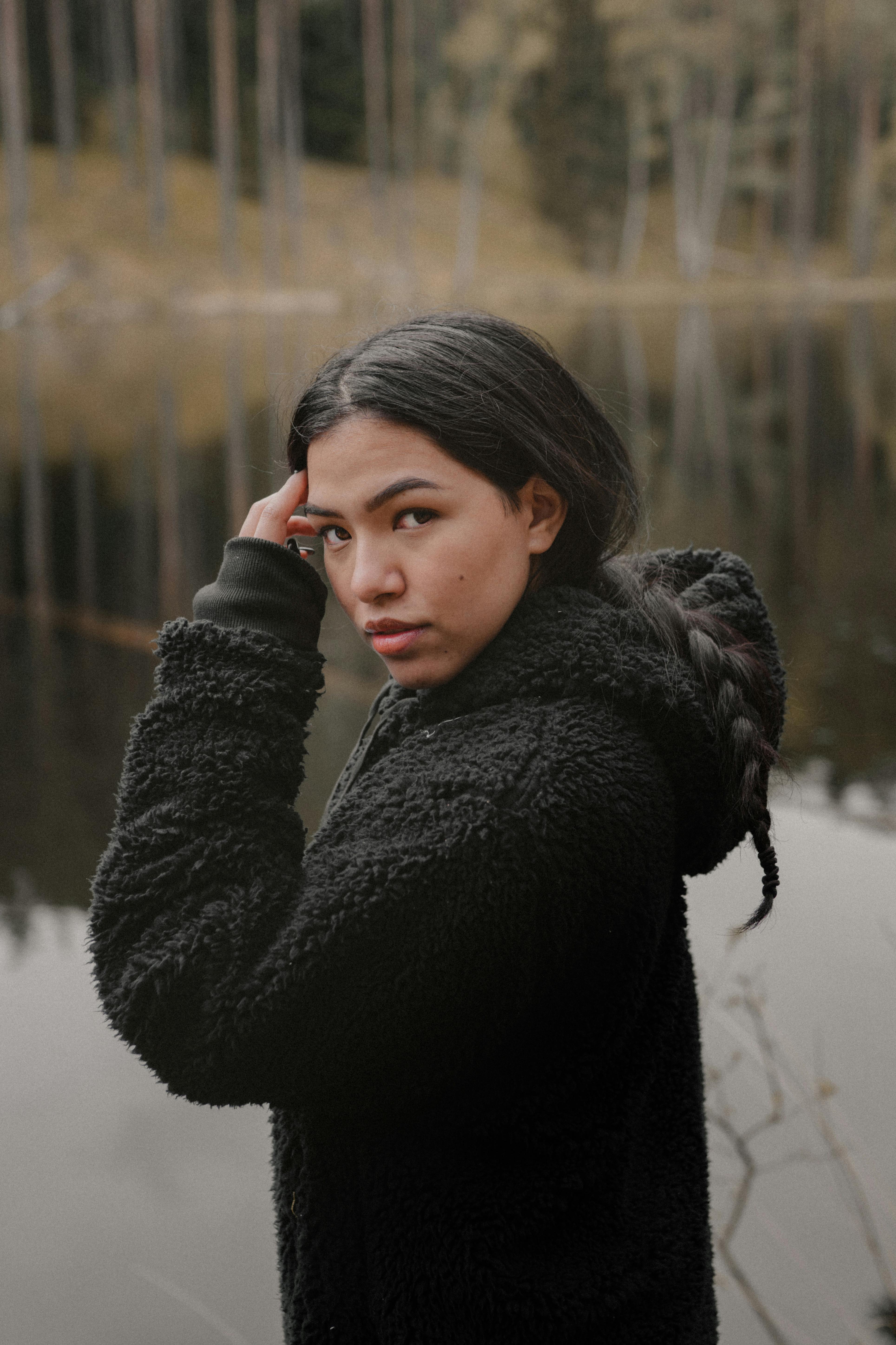 Beautiful portrait of a woman in a black hoodie by a tranquil lakeside, Lithuania.