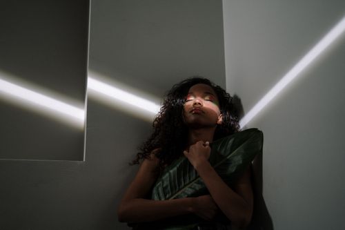Free Portrait of a woman with closed eyes holding a large leaf with dramatic light. Stock Photo