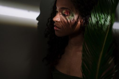 Free Artistic portrait of a woman with curly hair, playfully interacting with light and shadows. Stock Photo