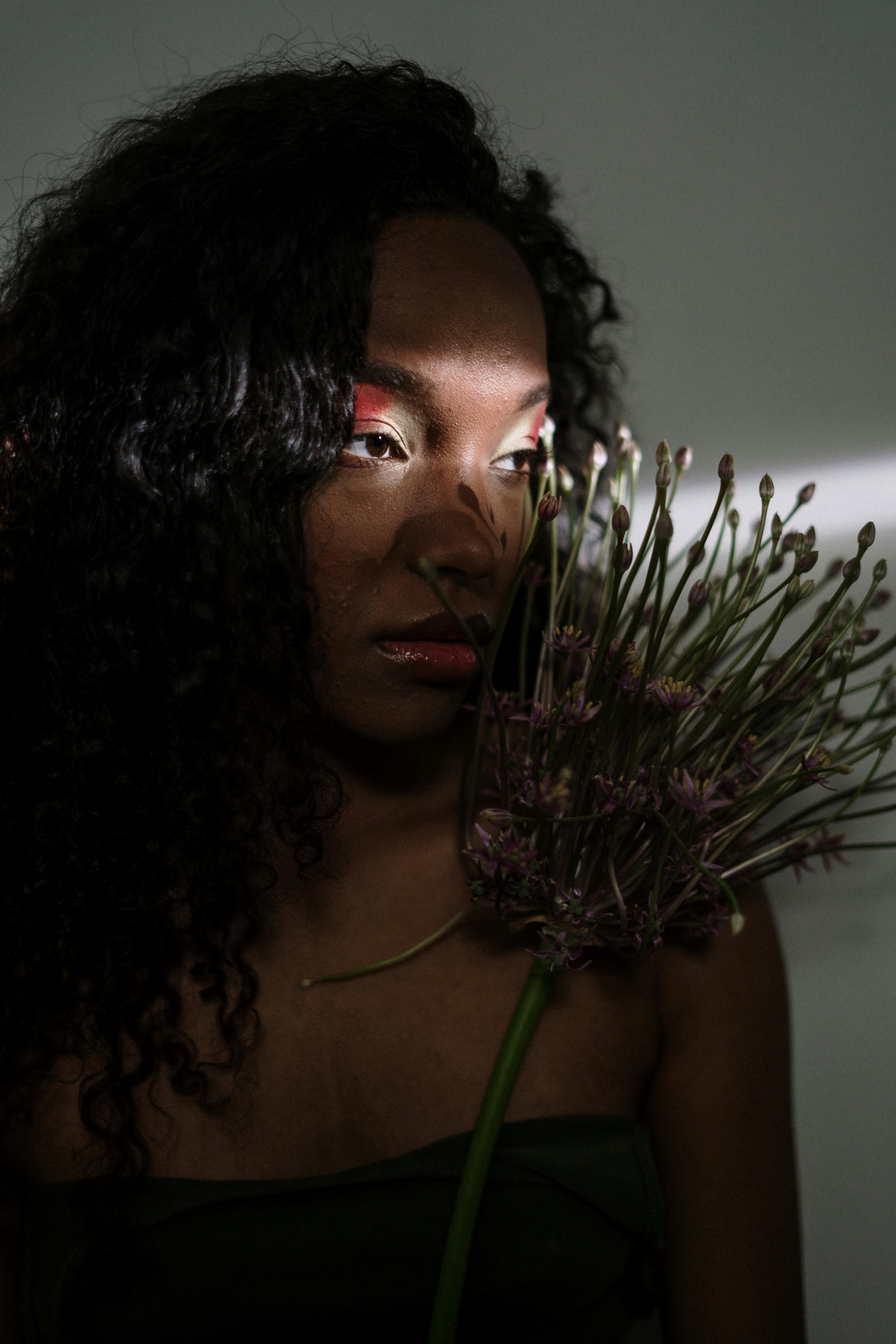 Stylish portrait of a woman holding a flower with artistic light effects emphasizing her face.