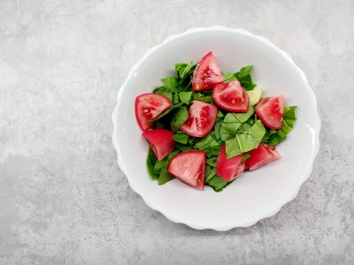 Free Top view of a fresh spinach and tomato salad in a white ceramic bowl on a gray surface. Stock Photo