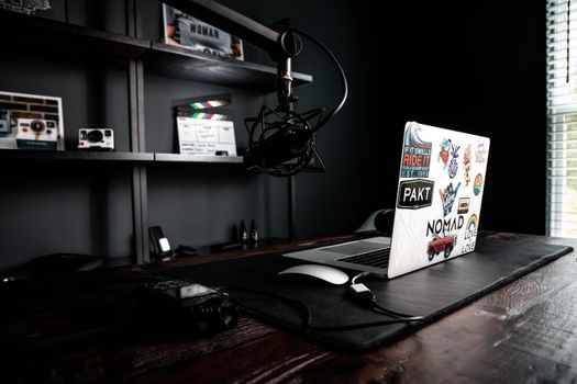 Contemporary style workspace with wooden table and open netbook with bright stickers near microphone and shelf with photo camera