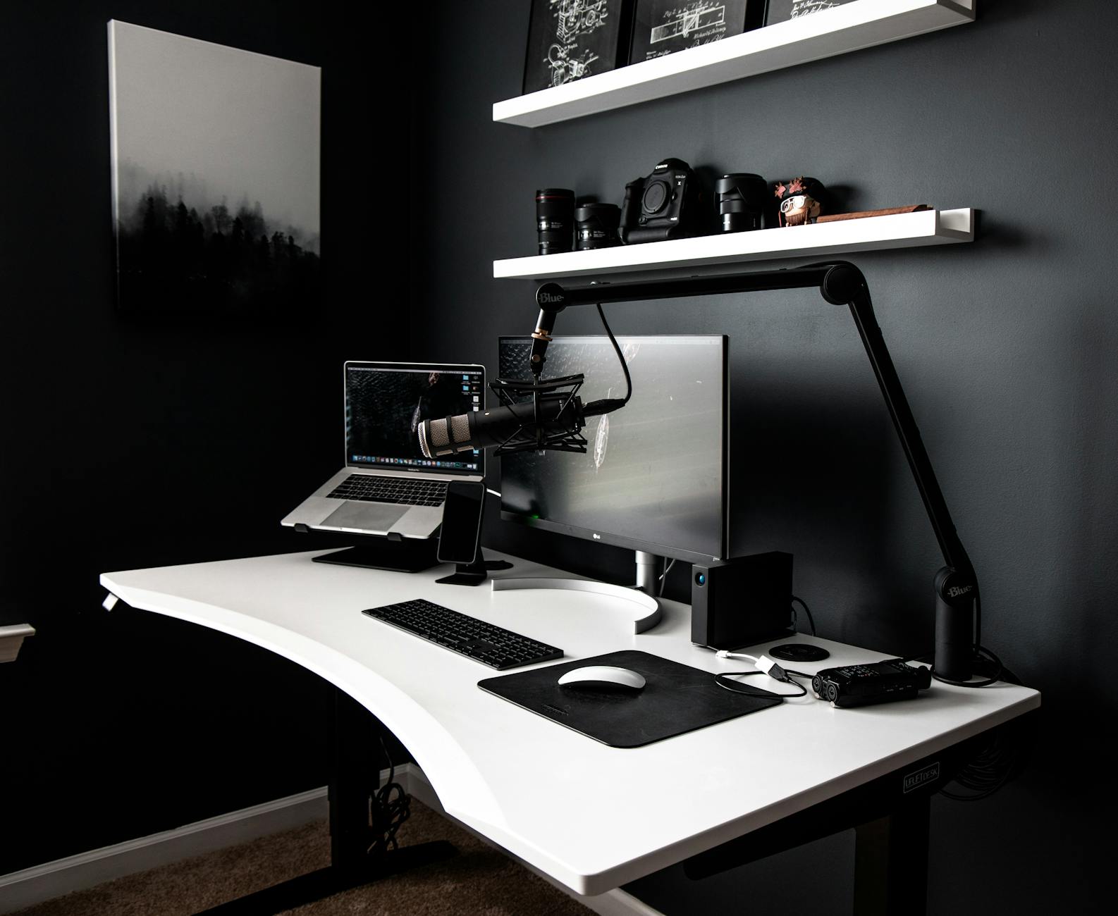 Contemporary style workspace with netbook near computer and microphone on white table in room with dark walls