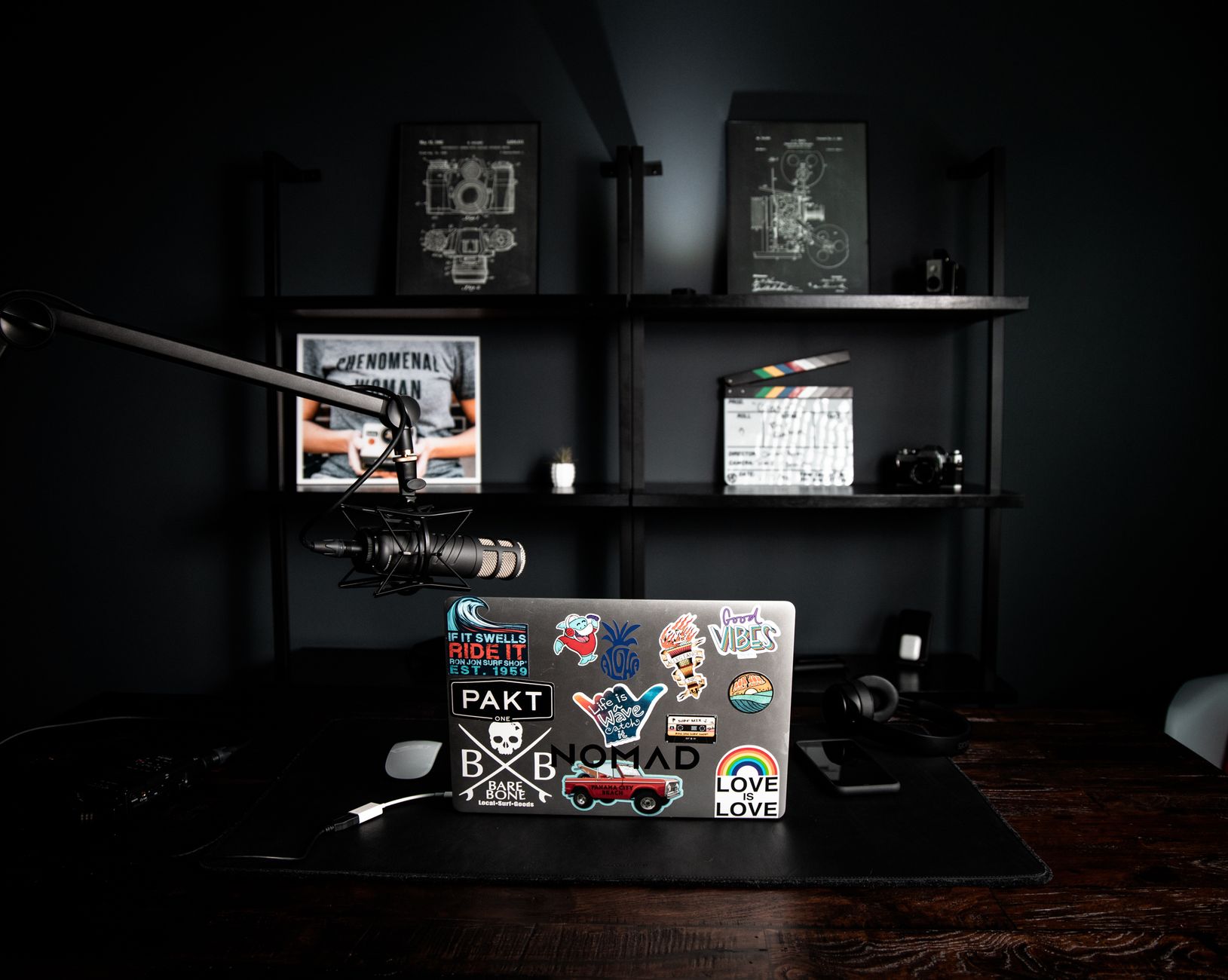 Creative design office interior with netbook with colorful stickers on table near dark shelf with schemes in frames and clapperboard
